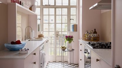 A small kitchen with pale pink walls and cabinetry and black and white checkerboard flooring