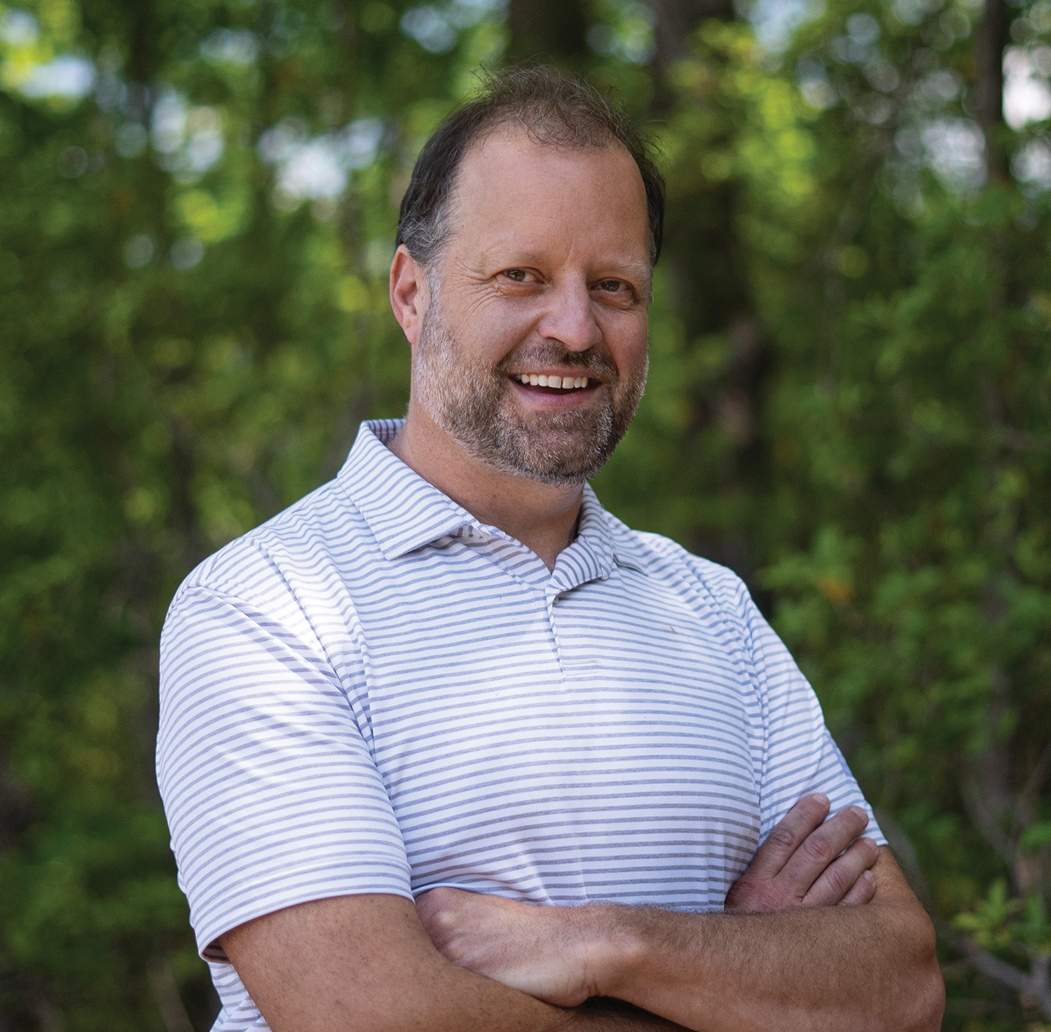 A headshot of a man in a striped polo shirt smiling at the camera
