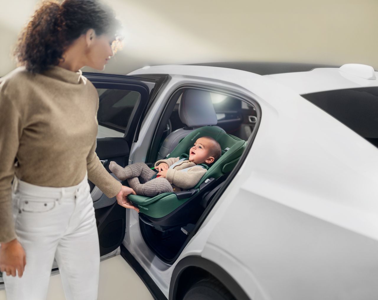 A smiling baby sits in a car seat while a young mum slides it out of the vehicle with ease