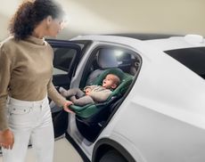 A smiling baby sits in an infant car seat while a mum slides it out of the vehicle with ease