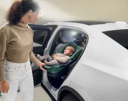 A smiling baby sits in an infant car seat while a mum slides it out of the vehicle with ease