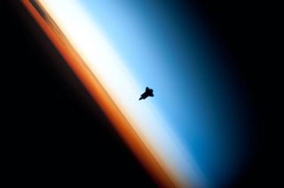 the silhouette of a space shuttle against earth's atmosphere in twilight