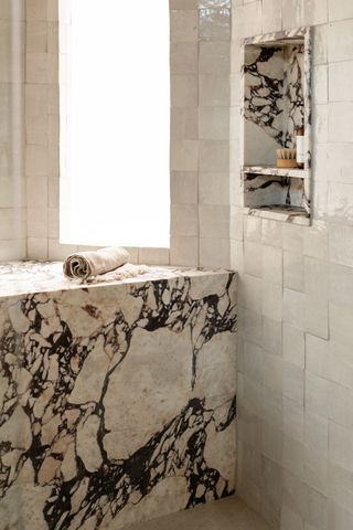 A white tiled shower featuring large pieces of purple veined marble