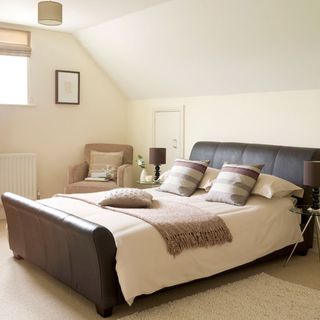 bedroom with cream colour wall brown bed with designed cushion