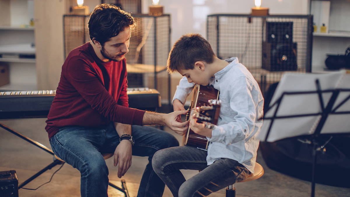 Man shows boy how to play the acoustic guitar