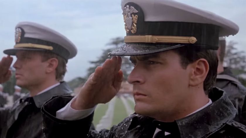 Charlie Sheen in the foreground wearing a navy dress hat and saluting