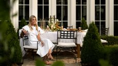 An outdoor lifestyle photograph of interior designer Shea McGee seated at a beautifully set dining table in a lush garden setting.