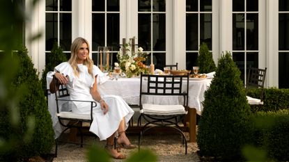 An outdoor lifestyle photograph of interior designer Shea McGee seated at a beautifully set dining table in a lush garden setting.