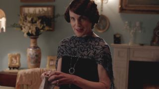 Elizabeth McGovern smiles coyly as she puts on a glove in the study in Downton Abbey.