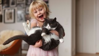 Young child holding black and white cat