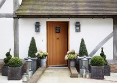 Front garden with stone paving leading to wooden door with topiary plants