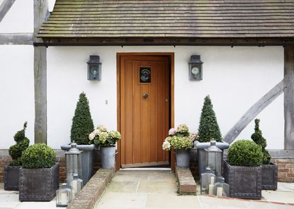 Front garden with stone paving leading to wooden door with topiary plants