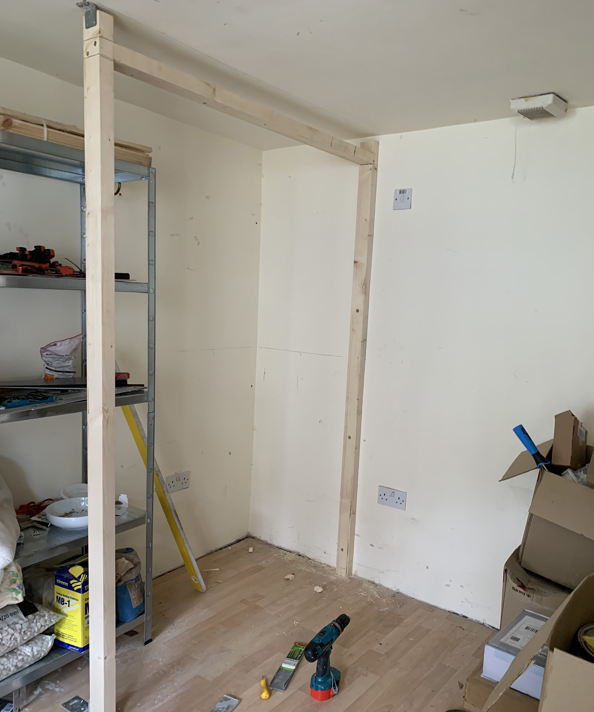 A wooden door frame in garden outbuilding with electric drill on laminate wood floor with metal open shelving