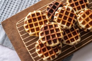 Golden waffles stacked on a cooling rack on a table top
