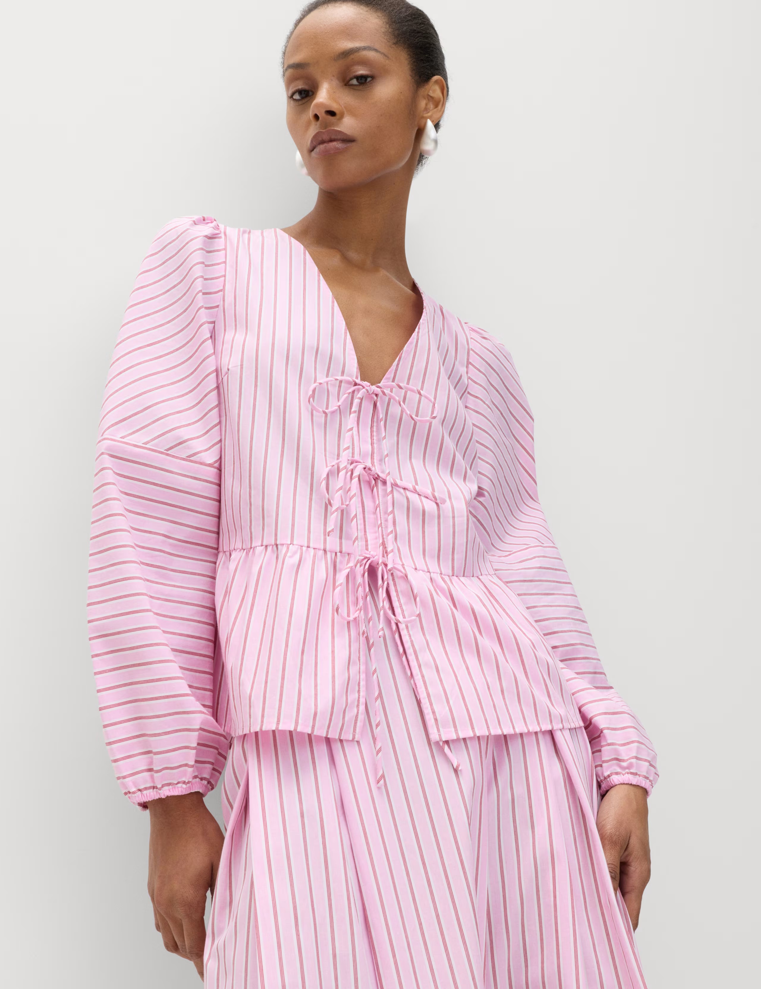 A model wearing a pink striped tie-front blouse.