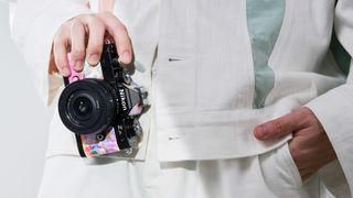 Man in white suit holding a Nikon Zfc camera with Heralbony graphics