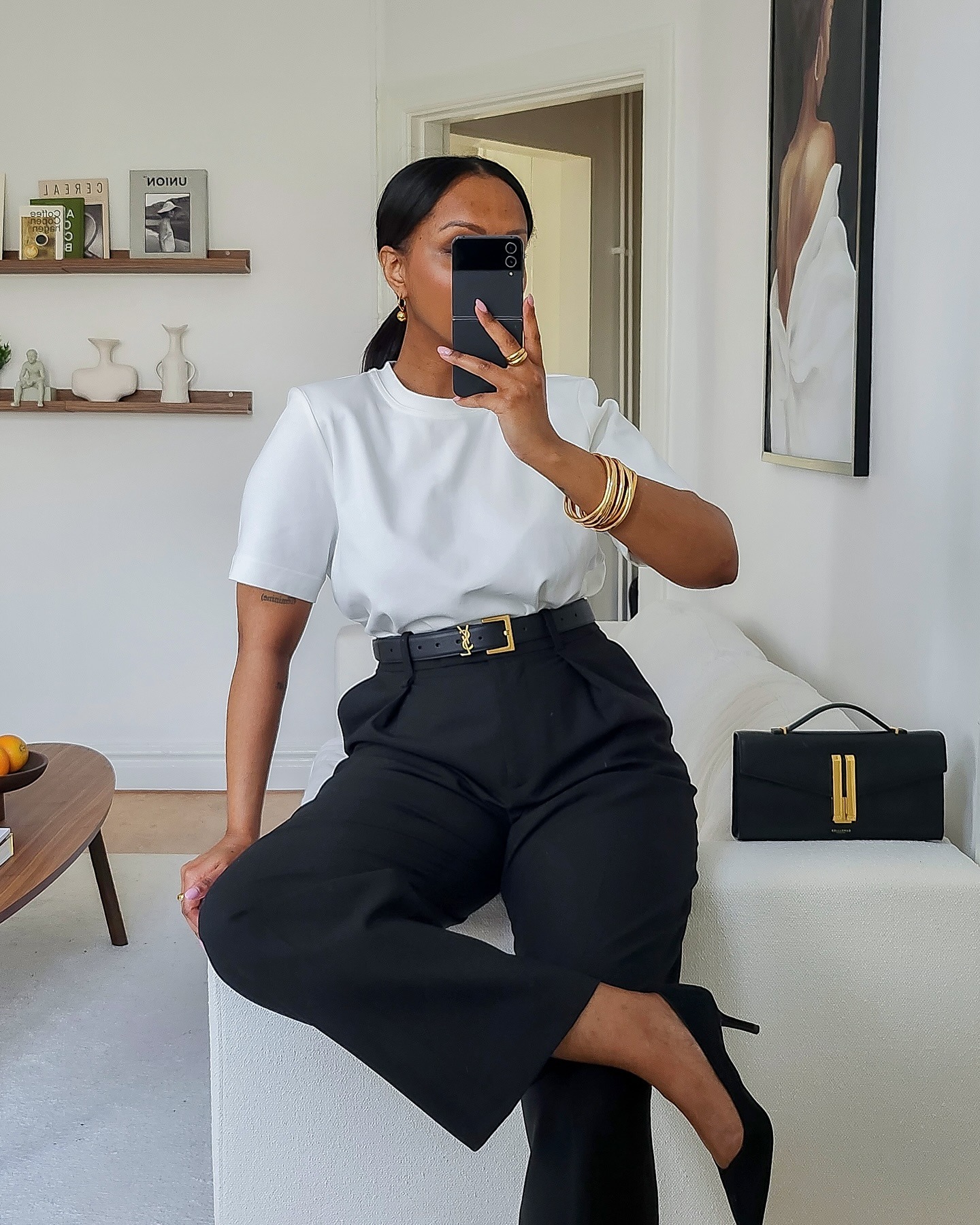 Woman wears white t-shirt, black tailored trousers, black belt saint laurent with cassandre