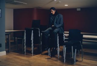 Man sat on pile of chairs in grey coat