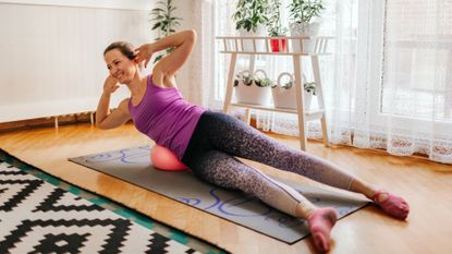 Woman exercising at home, lying on her side with her torso propped up on a small inflated Pilates ball