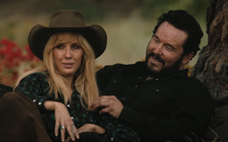 Beth in cowboy hat sitting with smiling Rip in the meadow in Yellowstone Season 5