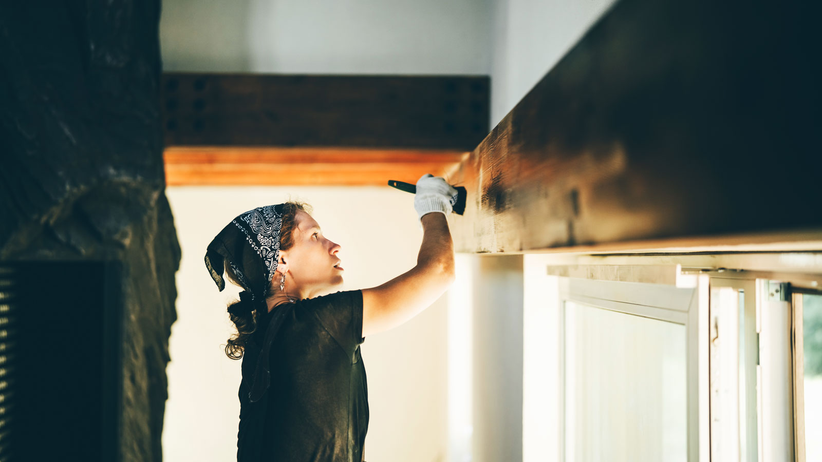 woman adding wood stain to wooden beam