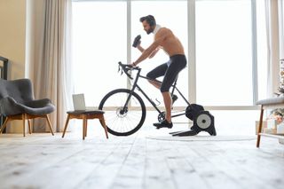 A white man rides a bike on a turbo trainer with headphones on