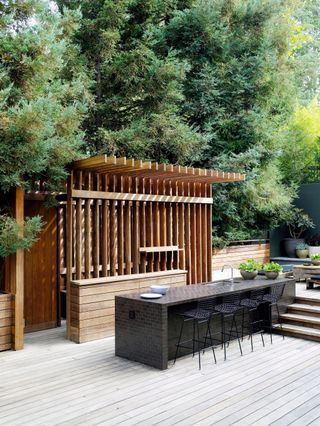 An outdoor kitchen with a wooden fence and bar-style seating