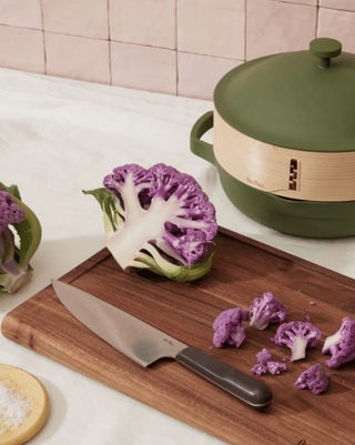 dark wooden chopping board with knife and broccoli on top and always pan to the side
