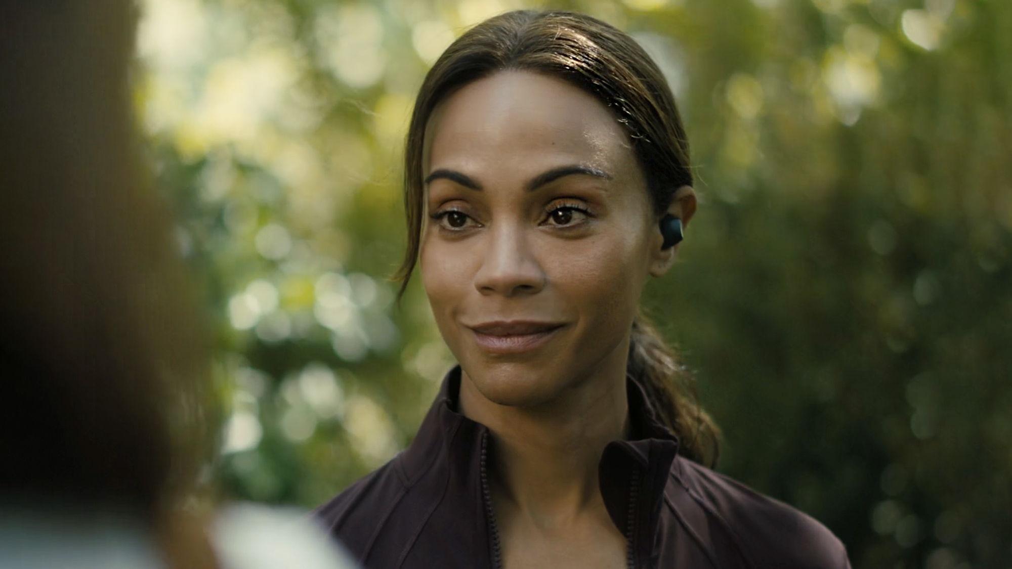 Zoe Saldana in purple sports gear and earbud in her left ear, starring in Lioness season 3 episode 1 (2026). 