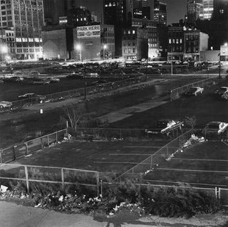 Black and white night image of an outside city parking lot with old American cars sparsely parked