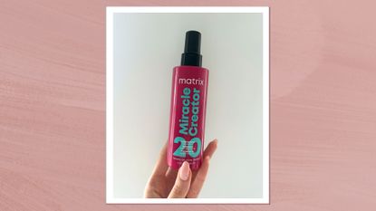 Image of hand holding Matrix leave-in conditioner on a mauve pink background