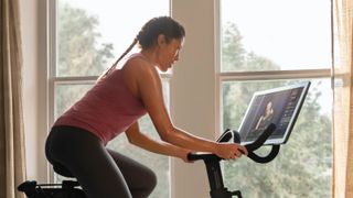 Woman riding on a Peloton bike in front of a large window