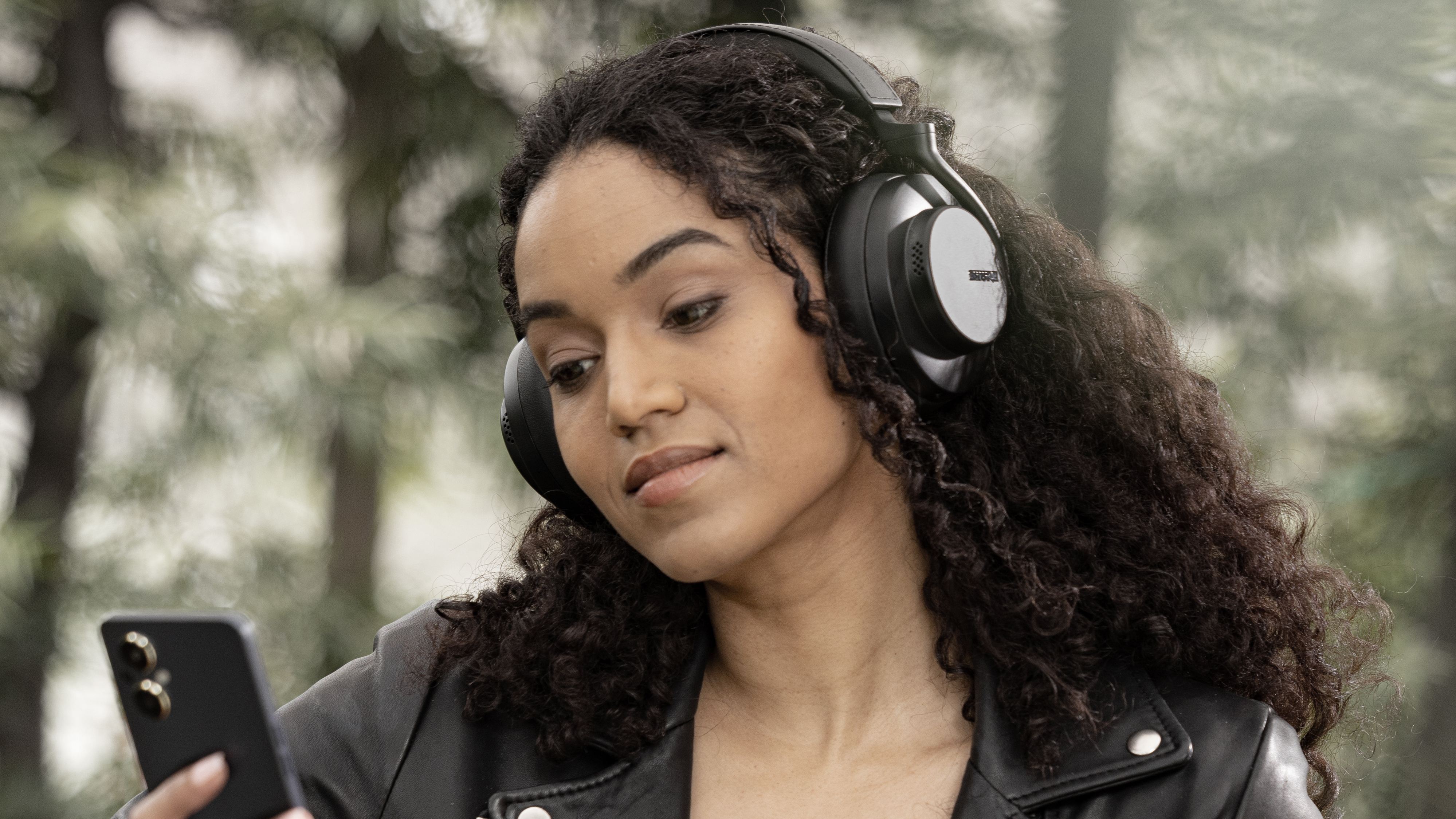 Shure AONIC Gen 2 worn by a womman outdoors who's looking at her phone