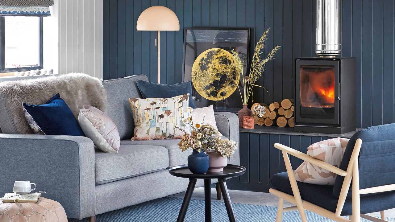 Midnight blue living room with panelled walls, a grey sofa and a fire burning in a wood burner