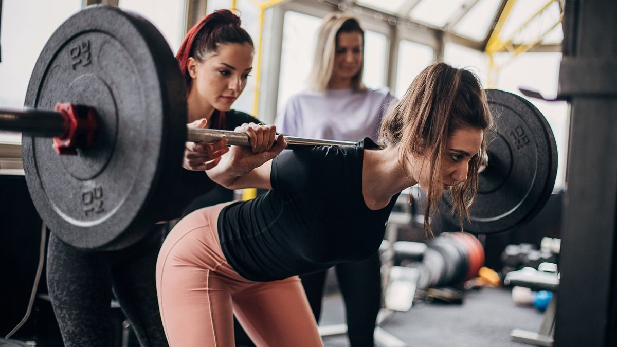 Woman performs good morning exercise with barbell