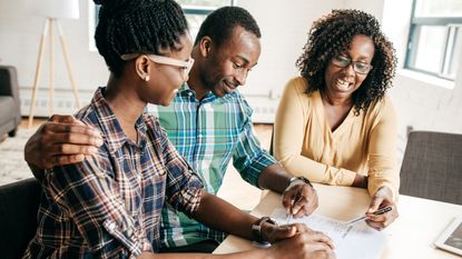 Three family members work on paperwork together while at a table. 