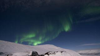 green bands of light reach out across the sky above a snowy mountaintop.