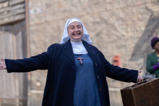 Sister Veronica (Rebecca Gethings) in a nun's habit stands in the street outside Nonnatus House with open arms in Call the Midwife.