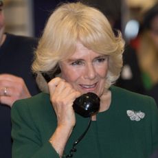 Queen Camilla talks on an old rotary phone while wearing a green dress