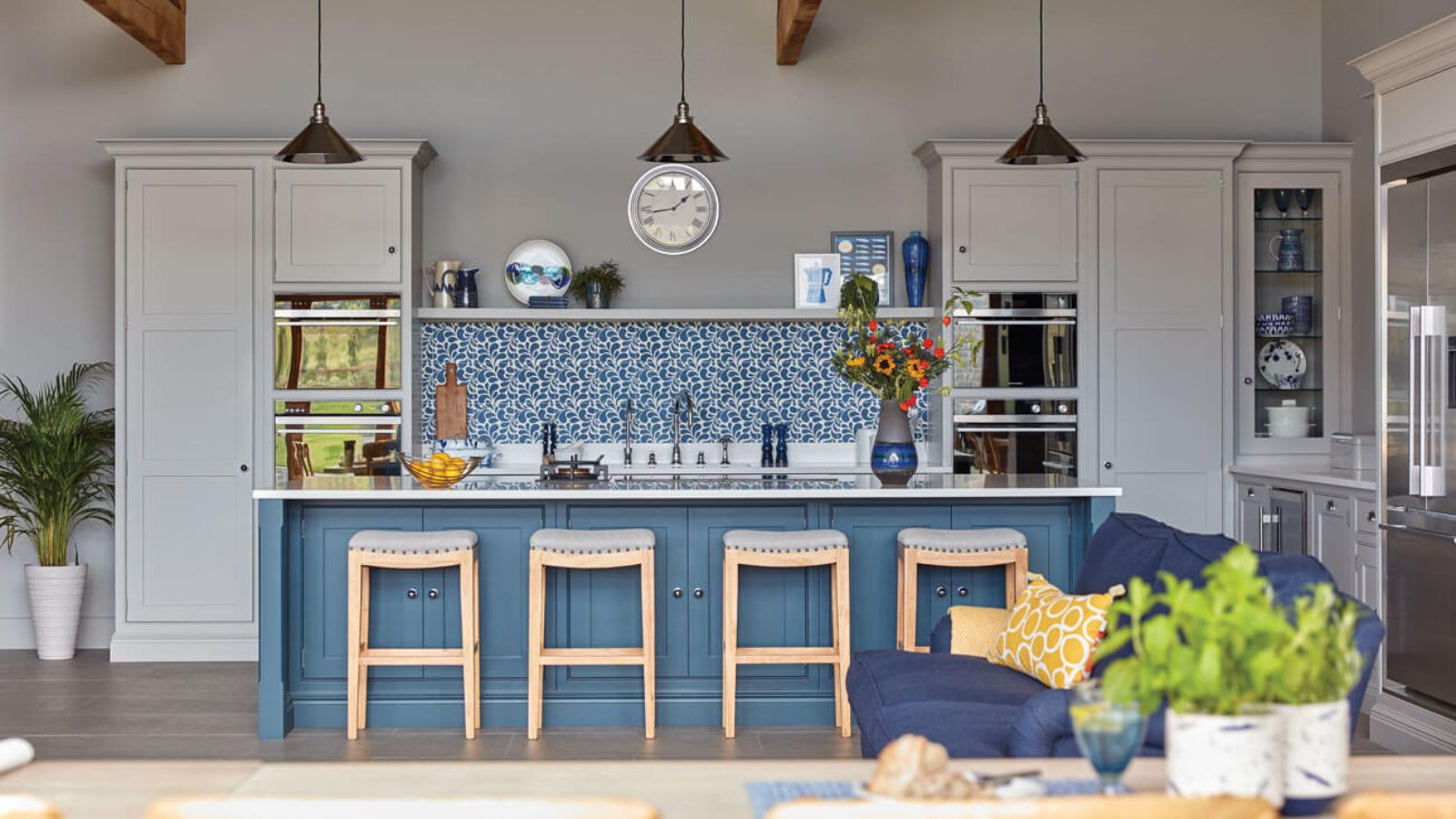 An open plan kitchen with a blue painted island, blue patterned tiles, and white cabinets. 