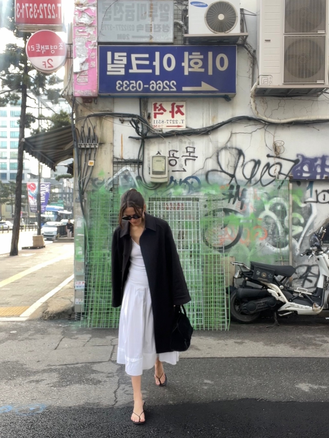 Eliza wears a black jacket, white dress, and flip flops.