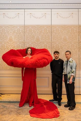 Two designers with model in dramatic red dress with giant neck ruffle