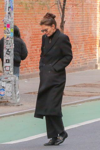 Katie Holmes walking in SoHo wearing a black coat and Gucci loafers