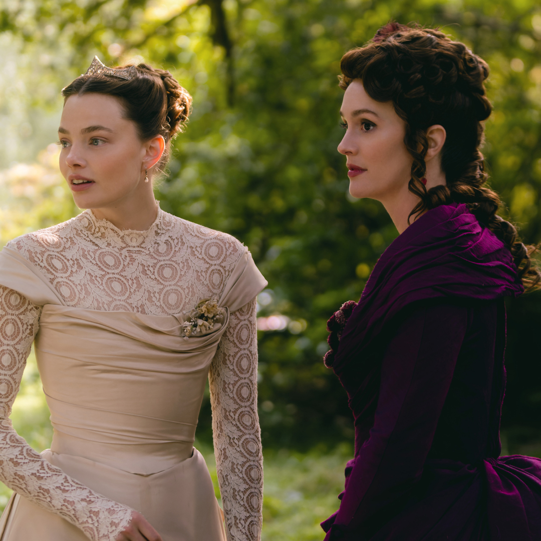 kristine froseth in a white dress and leighton meester in a purple gown speaking in a field in the buccaneers season 2