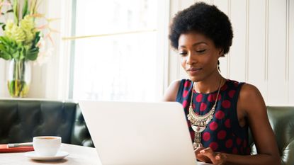 A woman grinning while reading her laptop.