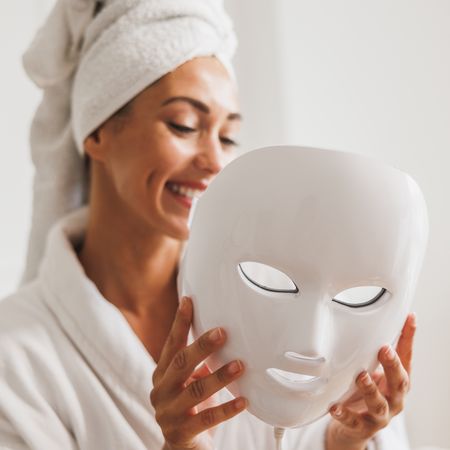 woman wearing hair towel and robe holding led face mask - the best beauty tech to buy at amazon