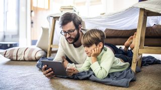 Man and son lying in blanket fort and using one of the best internet filter software on a tablet