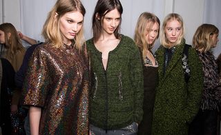 Five female models wearing looks from No 21's collection. One model is wearing a multicoloured sequin piece. Next to her is a model wearing a dark green zip cardigan and grey patterned bottoms. The third model is wearing a dark brown and blue embellished piece. The fourth model is wearing a dark green coat and dark coloured backpack with embellished straps. And the fifth model is wearing a dual coloured shaggy jacket