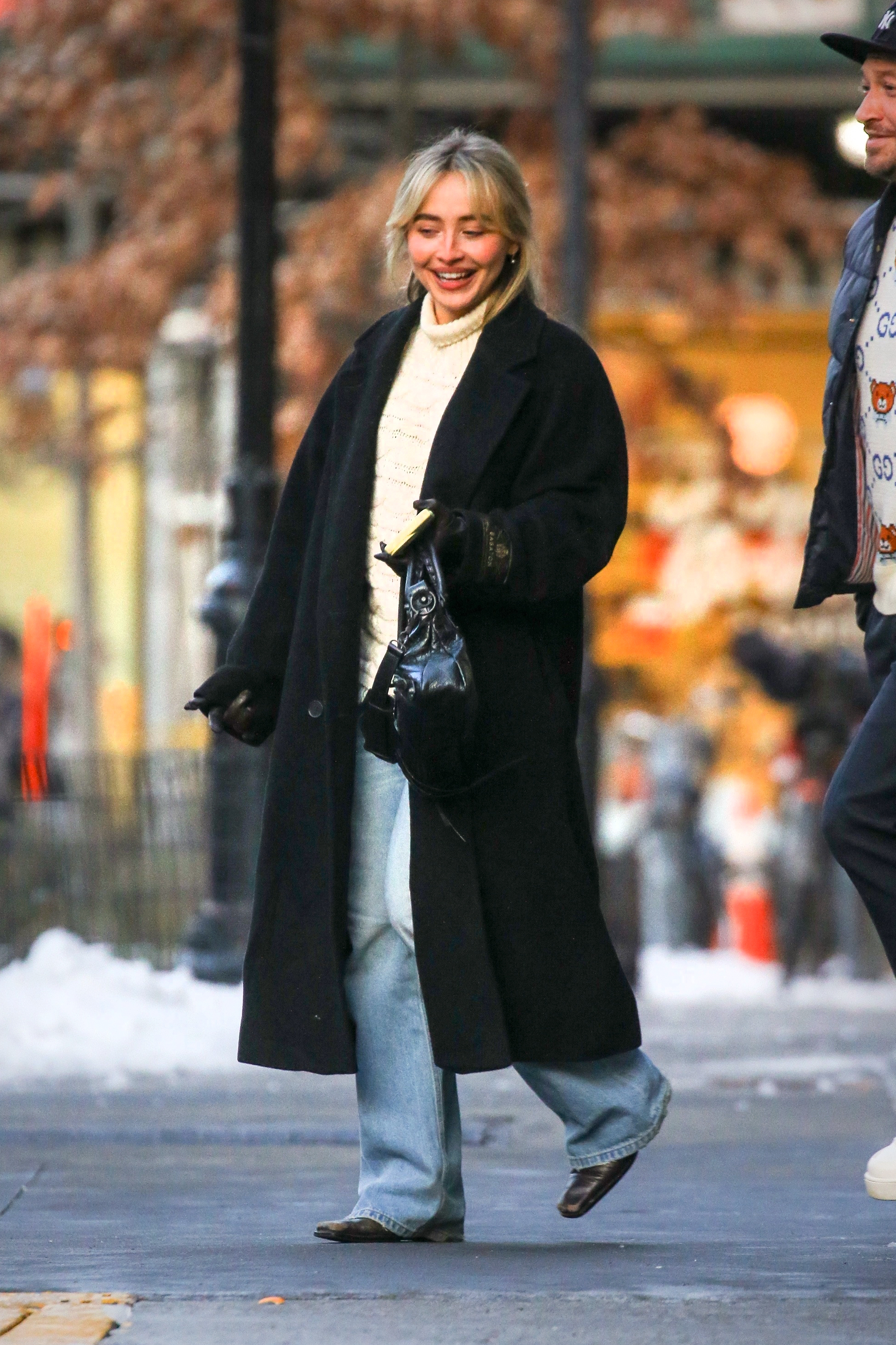 Sabrina wears a black wool coat, cable knit sweater, light-wash jeans, black boots, and a balenciaga bag.