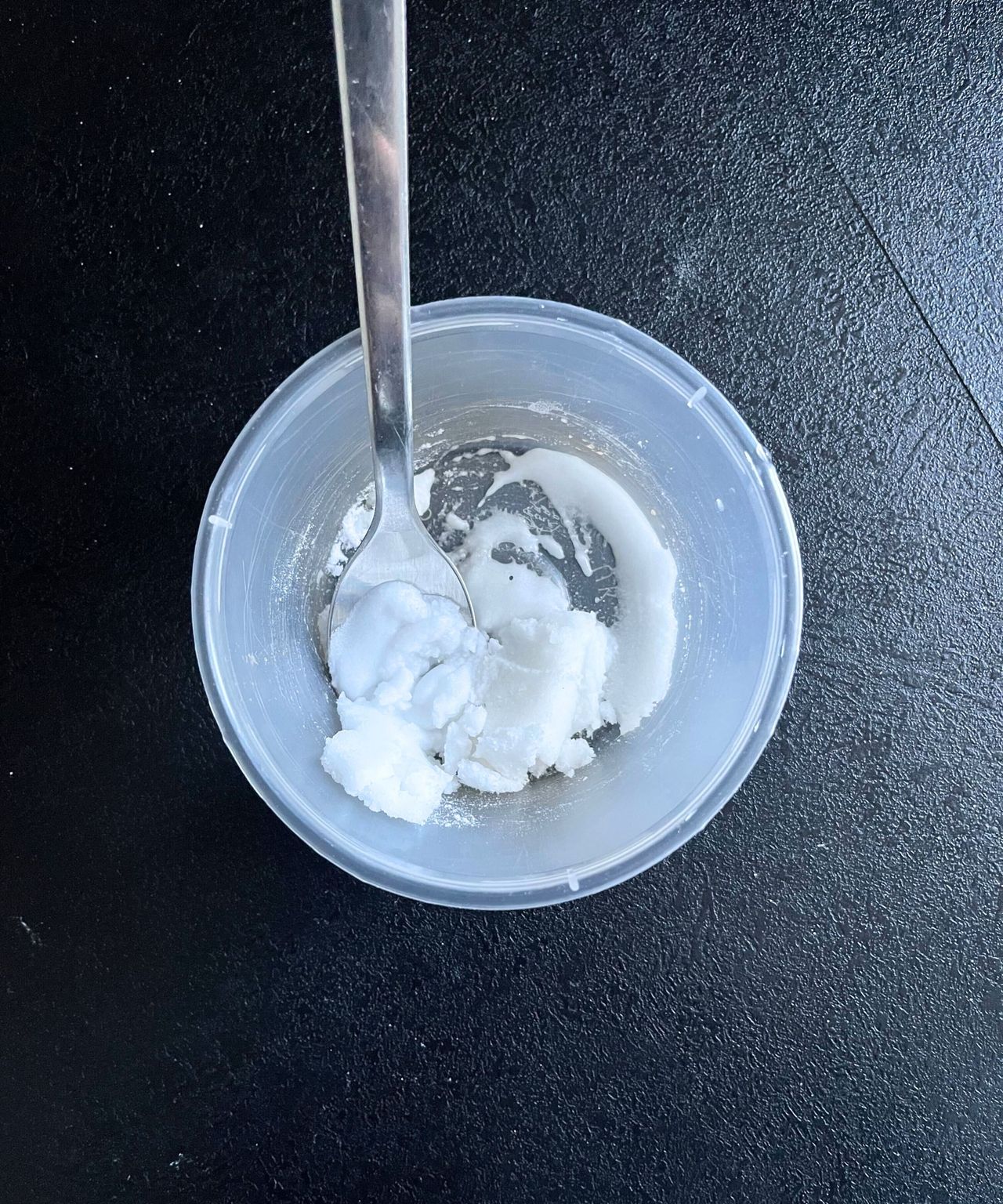 A thick, clumpy baking soda mixture in a round plastic container, with a silver teaspoon